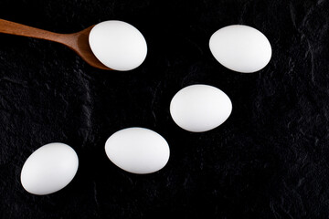 Raw white eggs and wooden spoon on black background