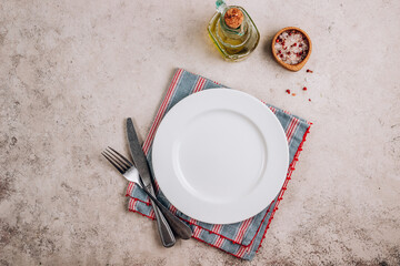 White plate, cutlery and napkin on stone table. Top view, copy space. Table setting. Background for menu
