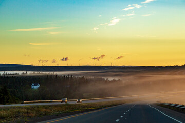 The early morning sunrise with a soft fog rolling across a rural highway.