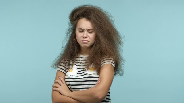 Stylish moody girl in striped t-shirt looking away, sulking and standing with crossed arms on chest, feeling angry at you, standing offended over blue background