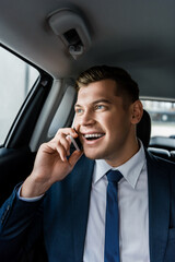Young businessman smiling while talking on smartphone on back seat of auto.