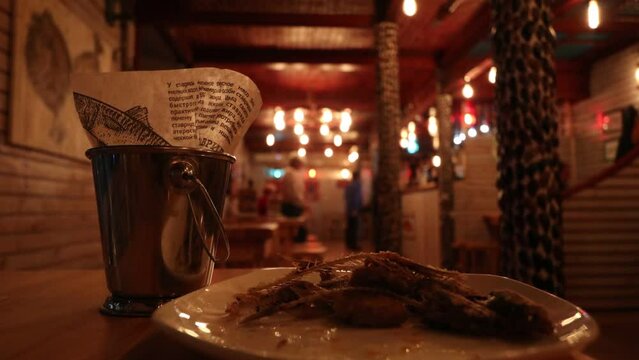 Fish bones on a plate. Fish on the table in the bar. Bar counter and bucket. Metal bucket with fish