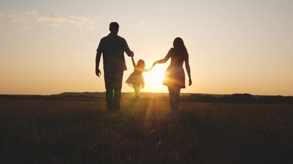 Fototapeta na wymiar Child plays with dad and mom on field in sunset light. Family and childhood. Little daughter jumping holding hands of dad and mom in park on background of sun. Walking with small kid in nature.