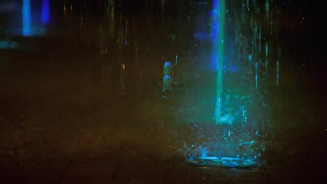 Splashes of fountain. Slow motion of water illuminated in colorful falling on fountain which change it water color in night. Wonderful multicolored fountain throws up high streams of sparkling water.