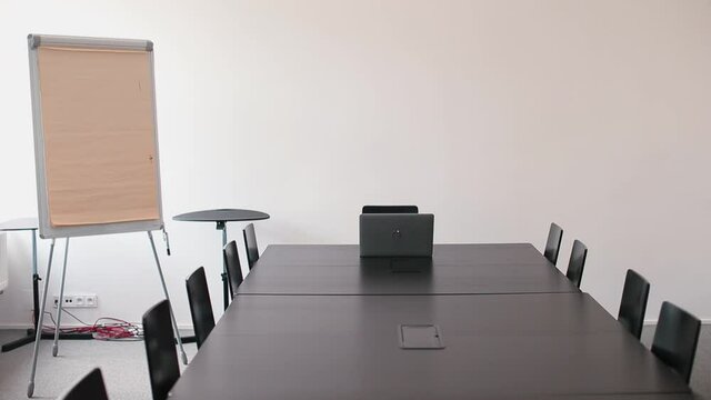 A female manager in a mask sits at an empty meeting table, working remotely using computer Internet technologies to communicate with the team. Digital adoption and transformation in business.