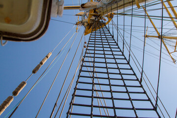 Obraz premium mast of a sailing ship against the sky. The sails have been removed. Rays, stairs, running rigging on the barge. day. Summer. Sunny.