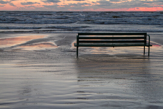Lonely bench on a deserted beach. Beautiful stormy sky. Sunset on the sea in rainy weather. - Powered by Adobe