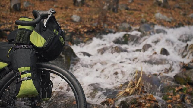 The mixed terrain cycle touring bike with bikepacking. The travel journey with light bicycle bags designed or modified for cycling. The trip on bike, outdoor in magical autumn forest, river stream.