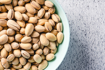 Top view close up on fresh salted roasted pistachios snack nuts in bowl with copy space on concrete table background