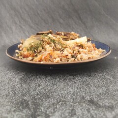 A blue plate with  an artichoke cutted in half with a quinoa salad side and a slice of lemon in a dark silver background