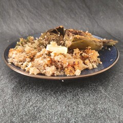 A blue plate with  an artichoke cutted in half with a quinoa salad side and a slice of lemon in a dark silver background