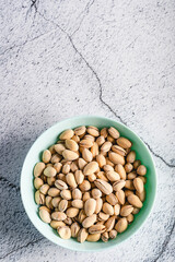 Top view on fresh salted roasted pistachios snack nuts in bowl with copy space on concrete table background