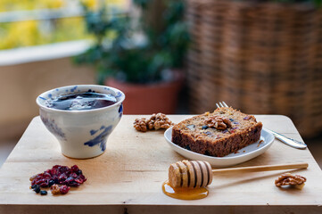 A slice of vegan cake with super fruit and nuts, honey and a cup of tea on wooden table.