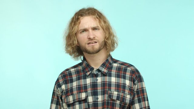 Slow motion of blond man with beard raising eyebrows surprised, hear something strange and looking confused, asking what and string questioned at camera, cant understand turquoise background