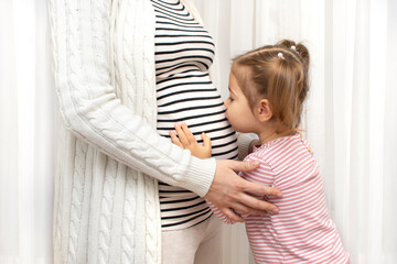 Pregnant woman with first daughter child. Cute and funny baby girl kissing and hugging her...