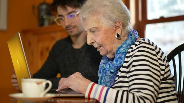 Extreme closeup of elderly senior woman learning to use a laptop computer from teen male grandson with tea.