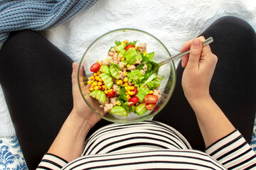 Cropped image of young hungry pregnant woman eating fresh tuna salad from glass bowl. Concept of healthy nutrition, vegetables and fish during pregnancy. Mother waiting baby. Omega 3 and vitamins.