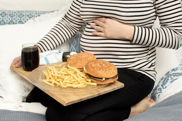 Cropped image of young hungry pregnant woman eating a hamburger and fried potatoes. Concept of...