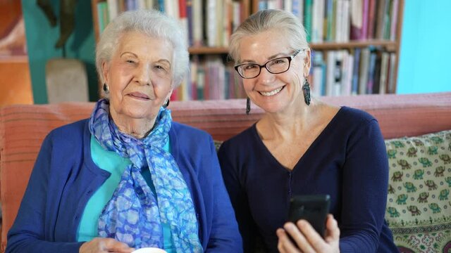 Portrait of elderly senior woman and mature woman drinking tea and looking at cell phone.