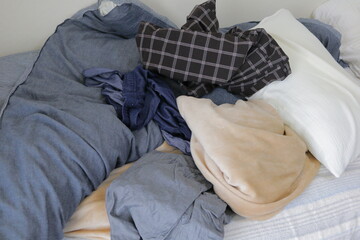 洋服が散らかった汚い部屋のベットと布団と枕
