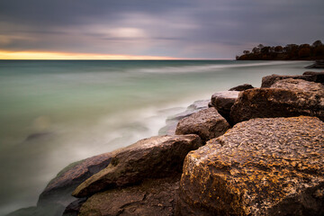 Long exposure photo of the rocky shores of Lake Ontario at sunrise