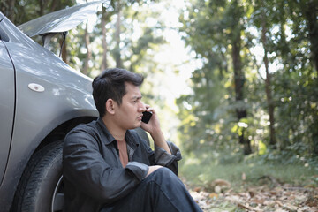 Man usea cellphone call garage in front of the open hood of a broken car on the road in the forest. Car breakdown concept.