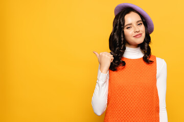  brunette woman in beret pointing with finger and looking at camera isolated on yellow