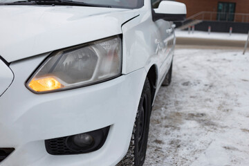 Fototapeta na wymiar A white car stands in a city parking lot in winter close-up. blurred focus