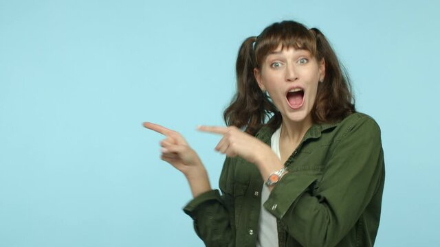 Slow motion of amazed brunette woman pointing fingers left at copy space, showing logo and looking impressed at camera, nodding approvingly, praise really good offer, turquoise background