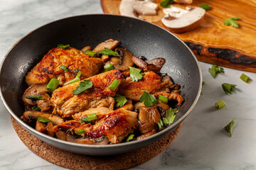 Side view selective focus image of sauteed roasted chicken breasts in a non stick frying pan on white marble seasoned with parsley, spring onion and mushroom as well as herbs, tomato sauce and spices.