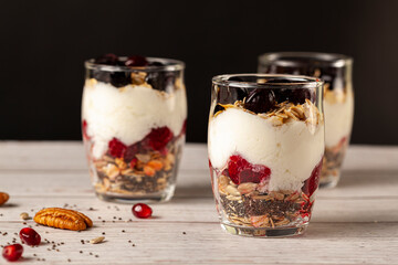 Side view of Delicious fruit and yogurt parfait  cups filled with layers of muesli, chia seeds, fresh berries, rolled oats, and homemade yogurt served with pomegranate and pecan on wooden background.