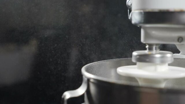 Cooking process. Electric mixer with metal bowl at work. Slow motion. Particles of flower on black background flying around. Pastry and bakery concept. Pasta, bread, Cake, cookies. Full hd