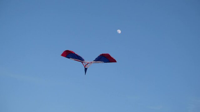 Slow motion of a kite flying high with the moon in the blue sky