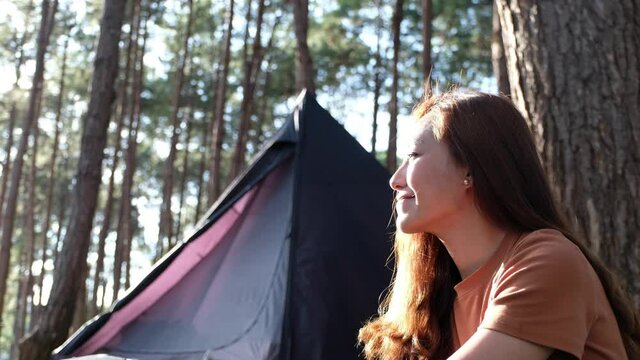 A young asian woman sitting next to a tent while enjoy camping in the outdoors