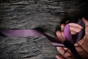Top view of male hand holding purple ribbon on wood background with copy space. Pancreatic cancer,...