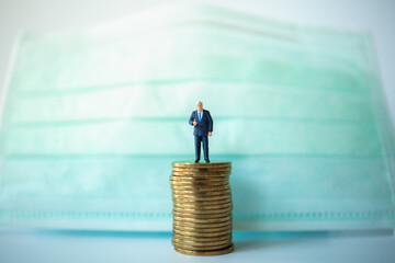 Money, Healthcare and Business Concept. Businessman miniature figure people standing on top of stack of gold coins with sugical face mask as background.
