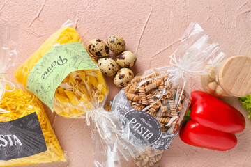 Bags with uncooked pasta, quail eggs and vegetables on color background