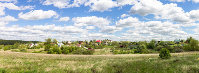 A lawn with green grass all the way to the horizon. Horizontal landscape of a flat field with fresh spring grass. Village, country houses, SNT, on the background of fields and trees.