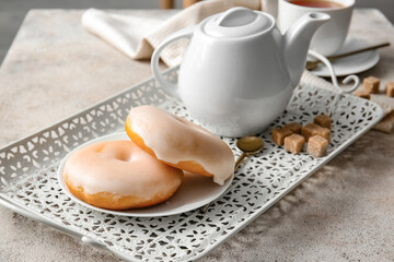 Plate with tasty donuts and teapot on table