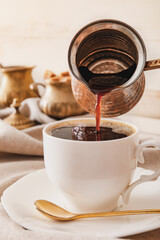 Pouring coffee from cezve in cup on table