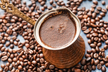 Cezve with hot coffee and beans on table
