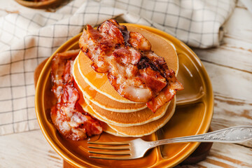 Plate with tasty pancakes and fried bacon on wooden table