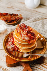 Plate with tasty pancakes and fried bacon on wooden table