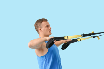 Fototapeta na wymiar Sporty young man training with TRX straps on color background