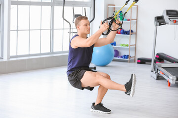 Sporty young man training with TRX straps in gym