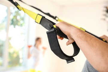 Sporty young man training with TRX straps in gym, closeup