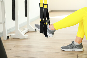 Sporty young woman training with TRX straps in gym