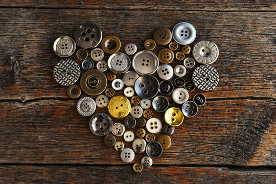 A top view image of old vintage buttons in a heart shape on an dark wooden table. 