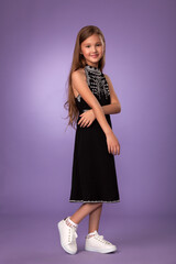 beautiful child girl in a stylish black dress with white embroidery and white beauties posing on a gray background