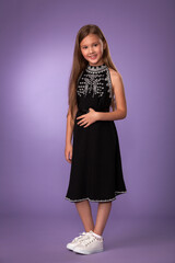 beautiful child girl in a stylish black dress with white embroidery and white beauties posing on a gray background